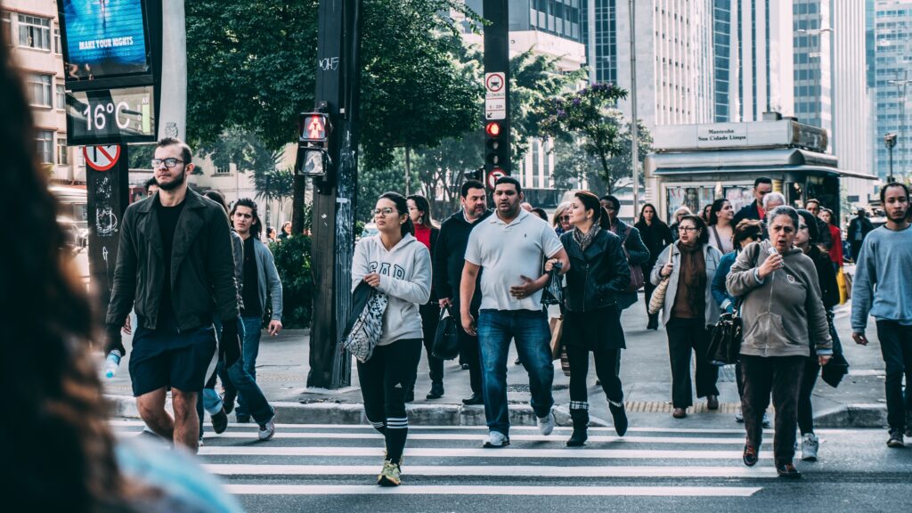 Cette phot montre une foule marchant dans un environnement urbain (feu avec passage pour piétons, immeubles...).