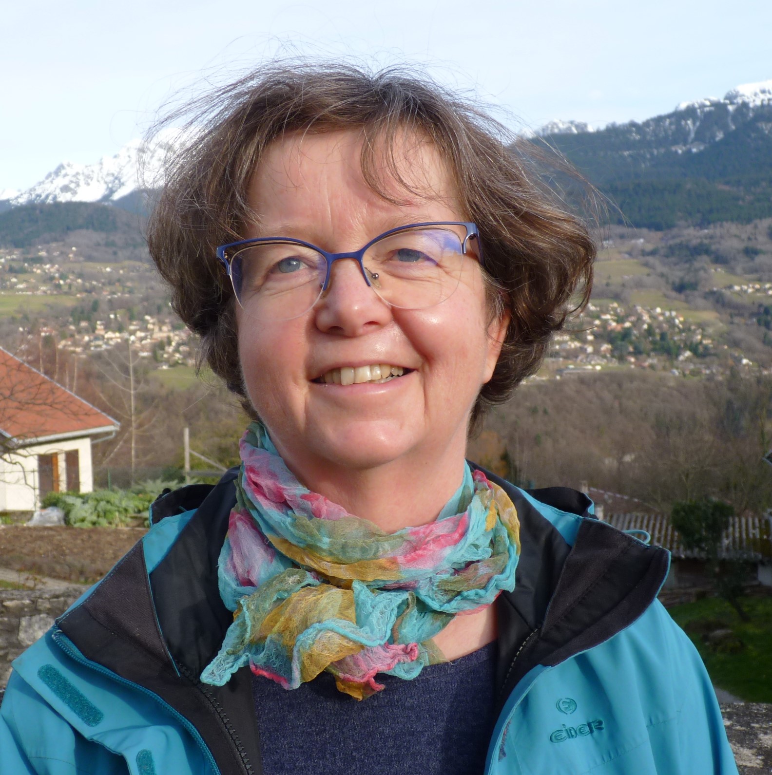 Cette photo montre le buste de Françoise Berthoud. Le fond de la photo montre un paysage de moyenne montagne.